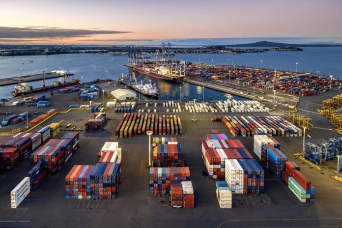Aerial view of Port of Auckland’s container terminal, with stacked containers, cargo vessels and cranes at dusk.